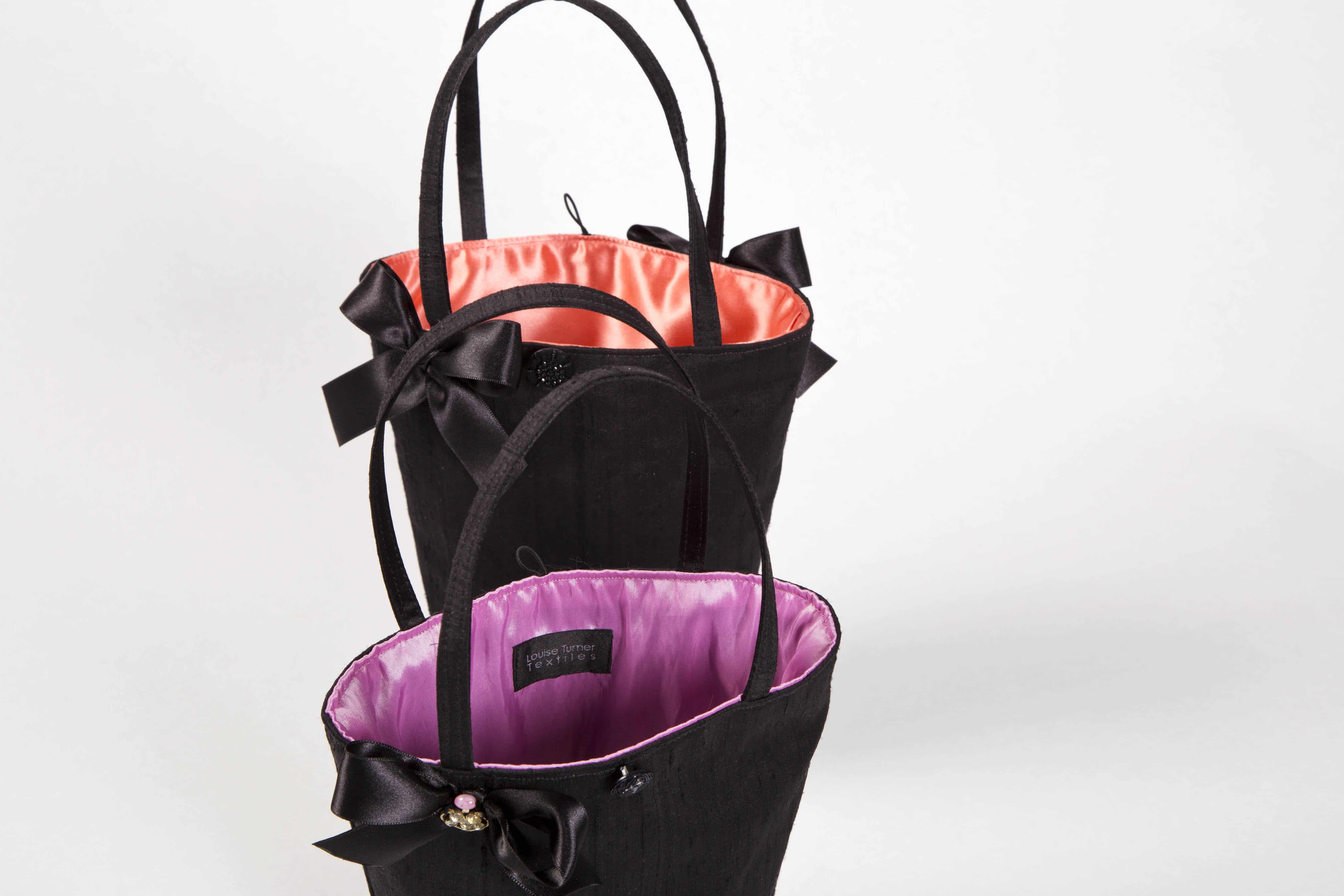 two black handbags with pink and orange linings